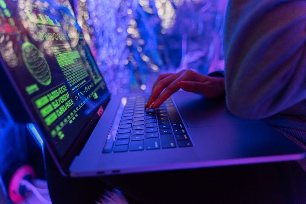 pexels-photo-5475752-5475752 Close-up of hands typing on a laptop displaying cybersecurity graphics, illuminated by purple light.